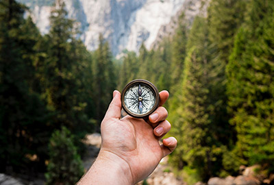 Photographie d'une main portant une boussole devant un paysage de montage